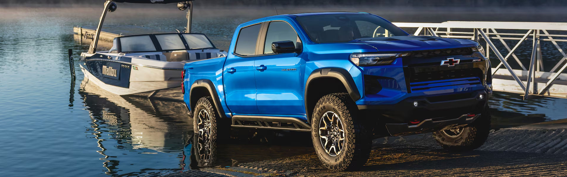 Bright blue Chevrolet Colorado ZR2 pickup truck towing a speedboat at a boat launch ramp.
